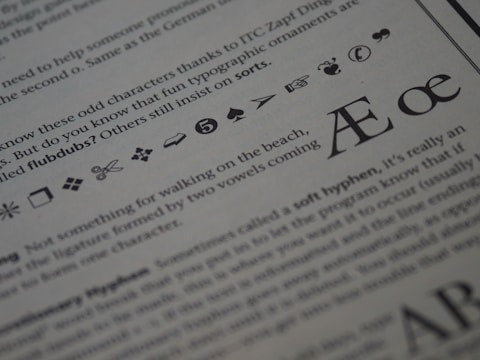 The image displays a close-up of printed text on a page. Various typographic symbols and special characters are highlighted, including a scissors icon, a hand pointing, and different shapes and icons such as arrows, hearts, and musical notes. The text is related to typography and typefaces, discussing characters and ligatures like Æ and œ.