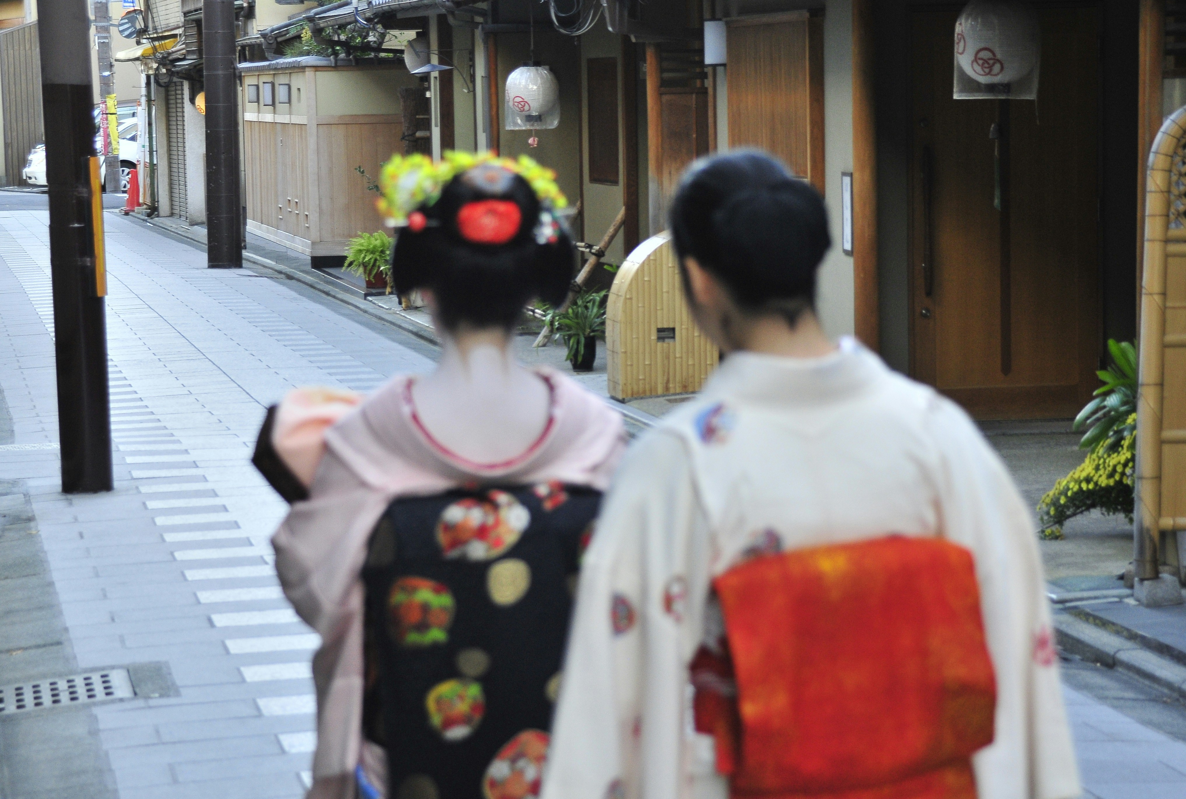 2 women in white and red floral dress walking on sidewalk during daytime, Ghosts.</p><p>The lady with the flowers in her hair is a maiko and she is absolute top in Kyoto. She comes as close to perfection as possible. A maiko is an apprentice geiko. And since this is Kyoto, it