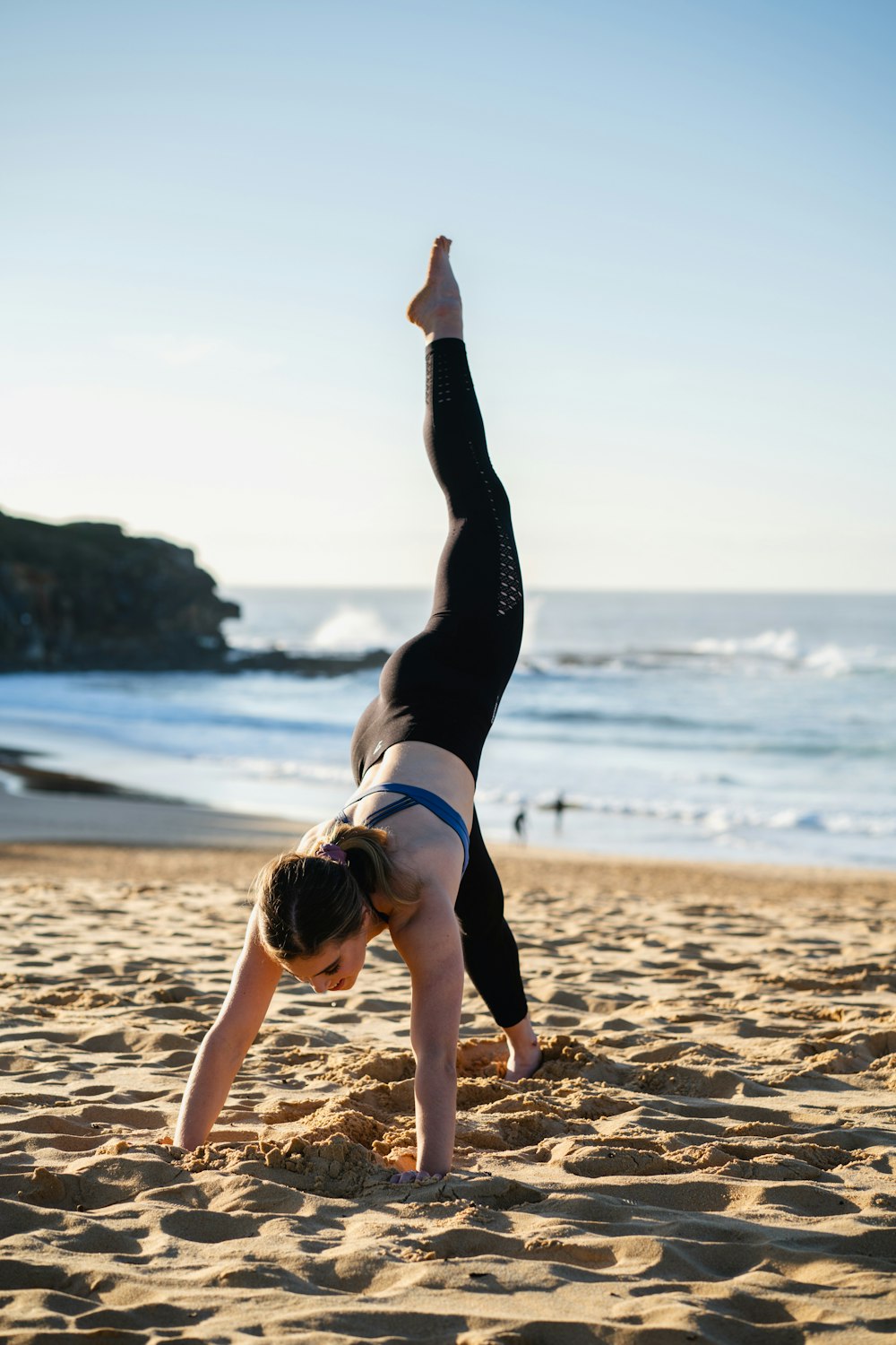 donna in reggiseno sportivo in bianco e nero e leggings neri che fanno yoga sulla spiaggia durante