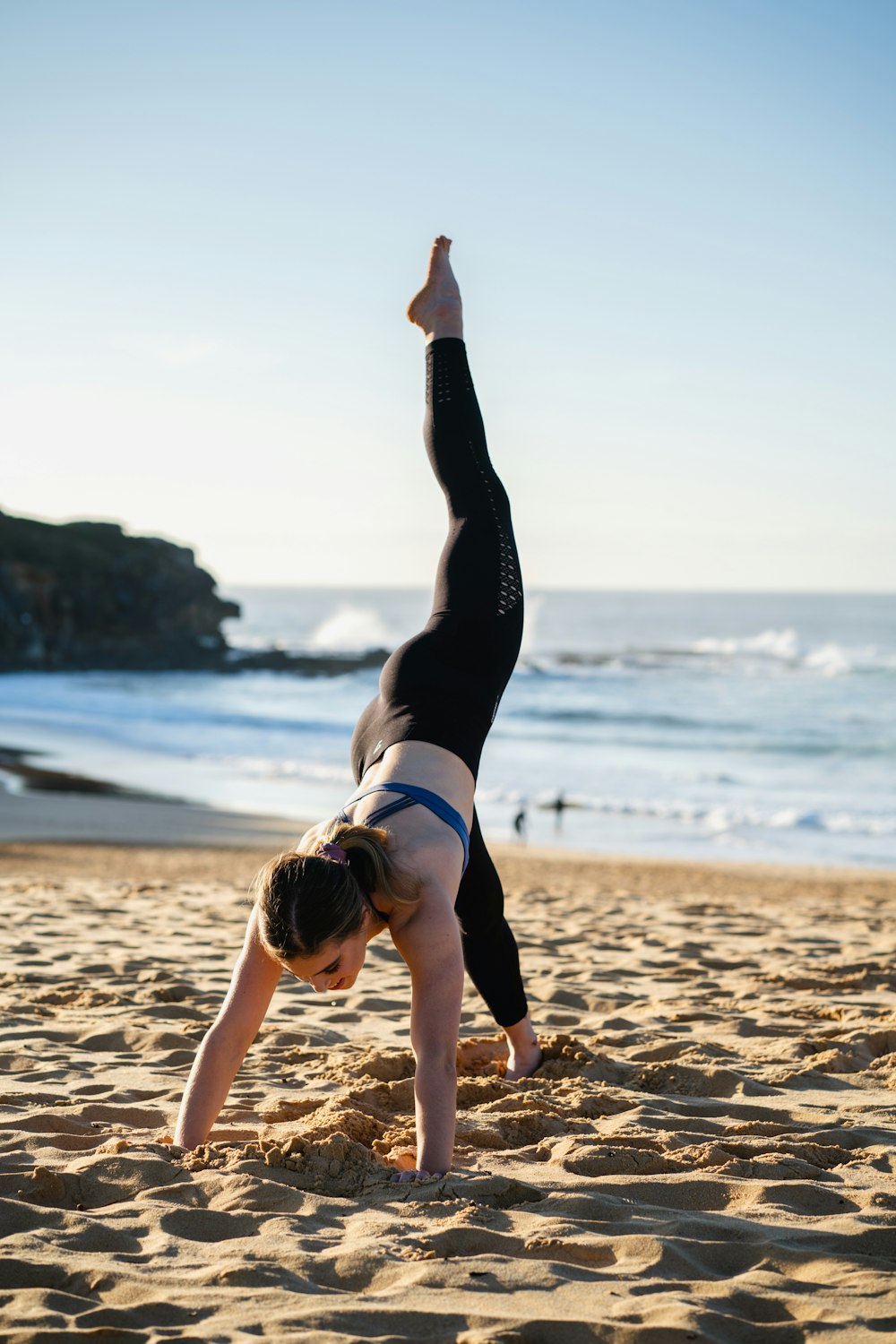 mujer en sujetador deportivo blanco y negro y polainas negras haciendo yoga en la orilla de la playa durante