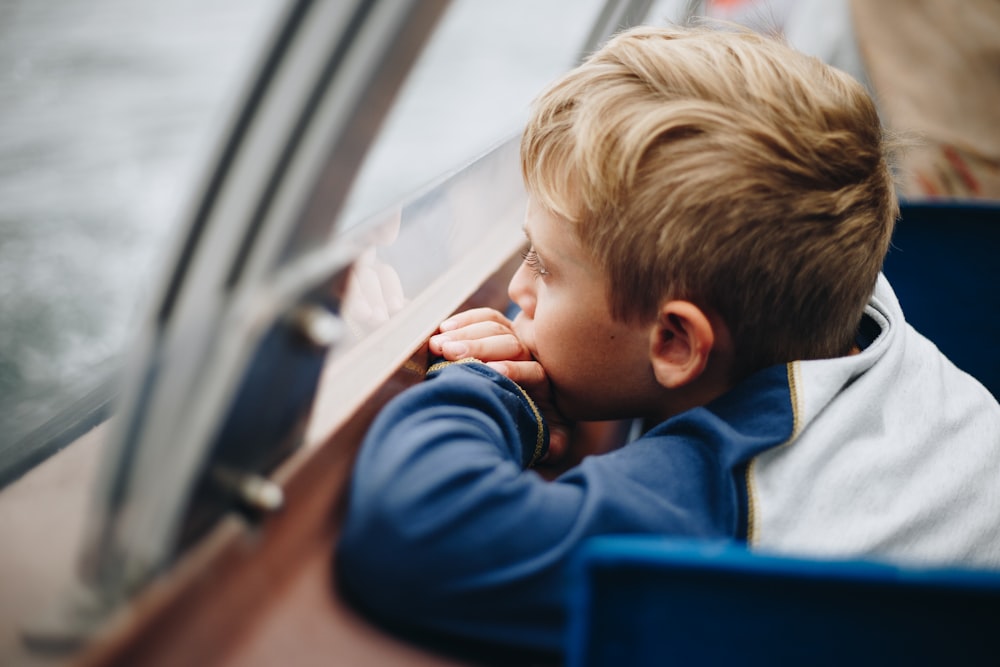 boy in blue long sleeve shirt looking out the window