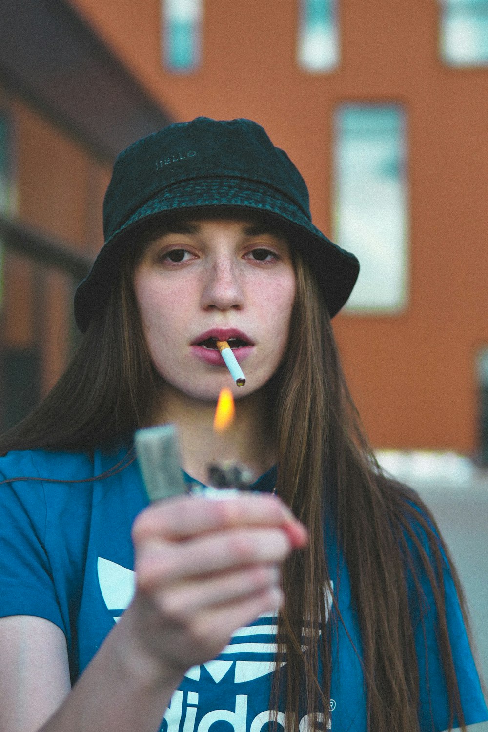 woman in blue shirt holding white disposable cup with lighted cigarette stick