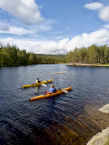 yellow kayak on body of water near green trees under blue and white cloudy sky during