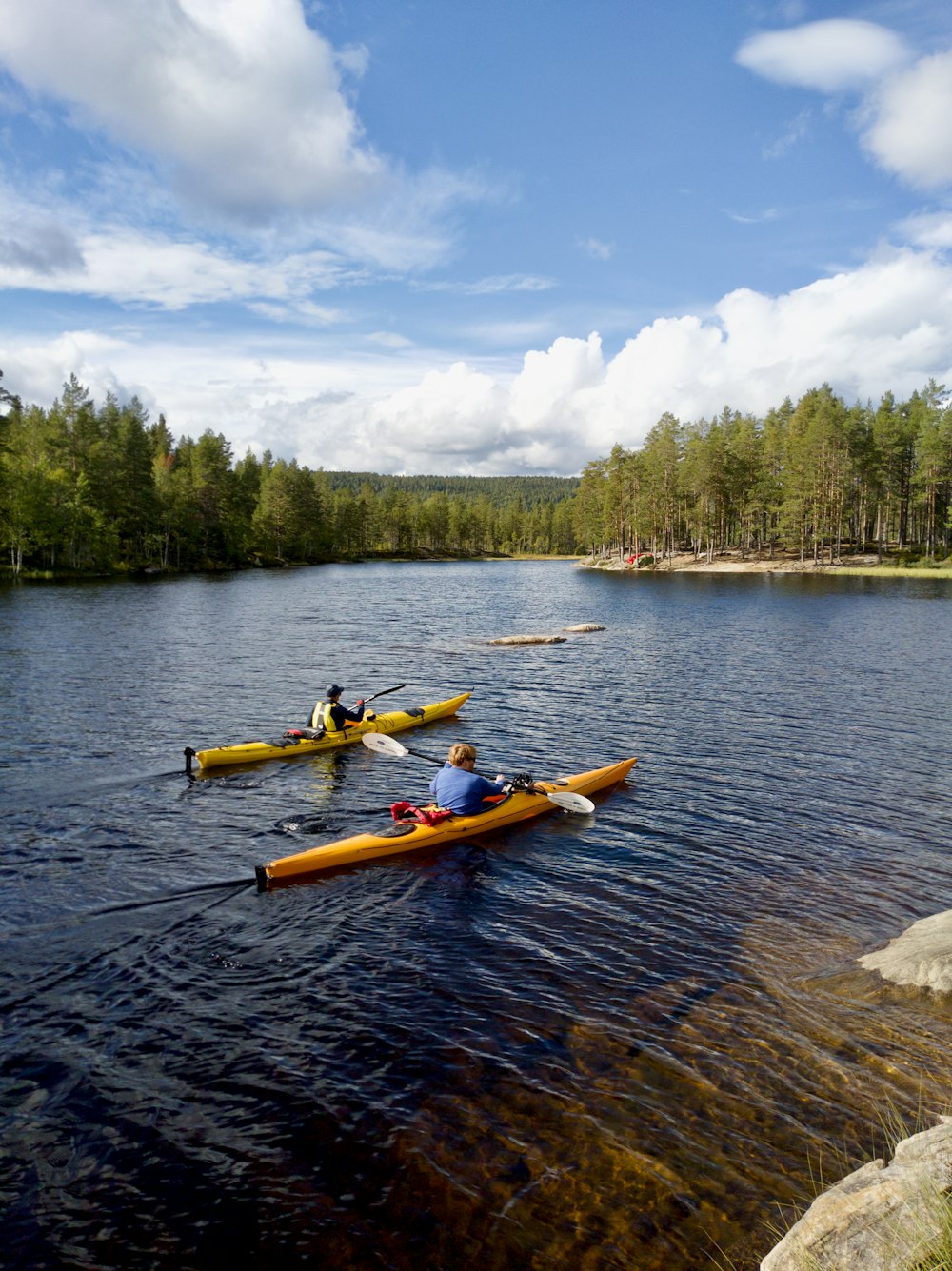 yellow kayak on body of water near green trees under blue and white cloudy sky during