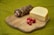 A wooden cutting board displays a piece of hard cheese, a roll of cured meat, and several small red radishes. The background is a green fabric, complementing the rustic presentation of the food items.