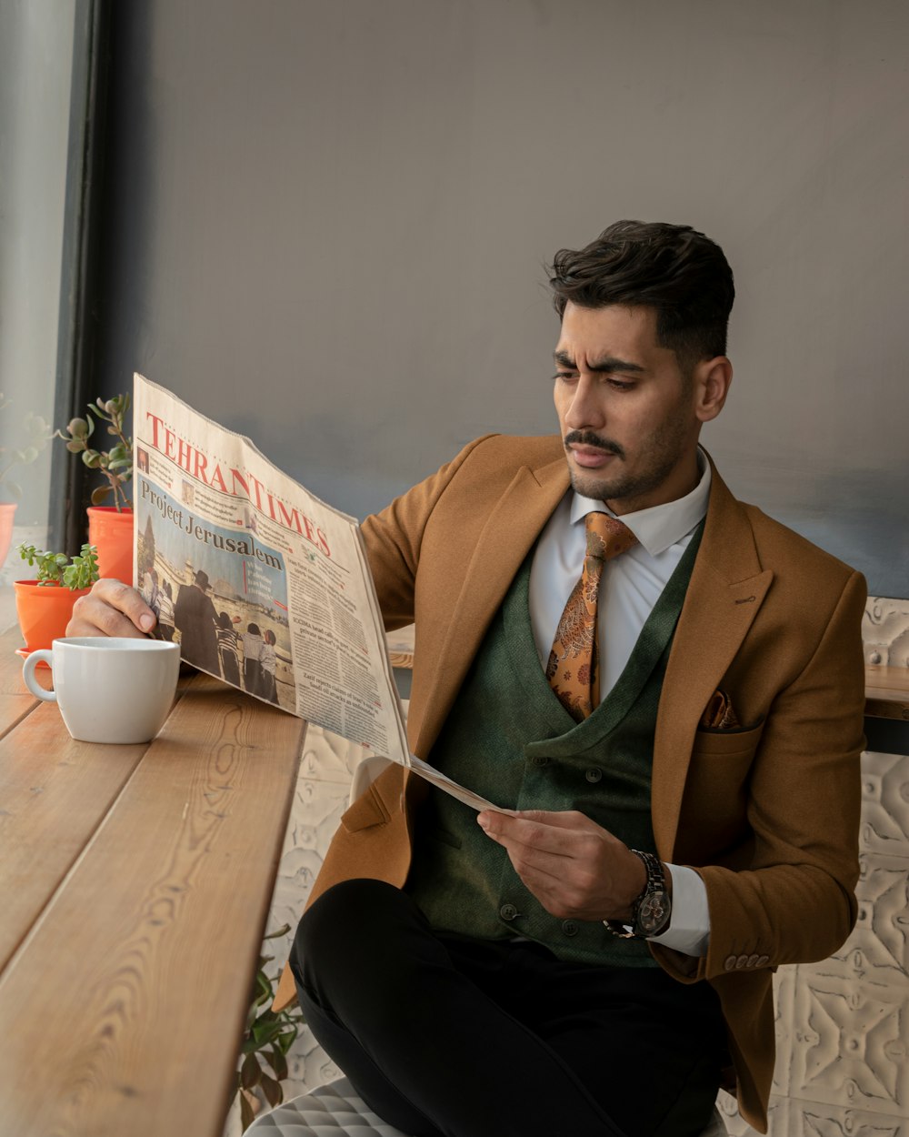 man in brown suit jacket sitting by the table