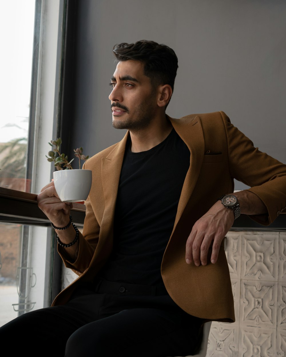 homme en blazer marron tenant une tasse en céramique blanche