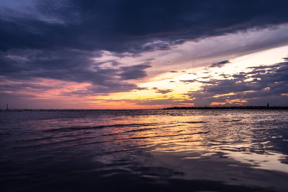 body of water under cloudy sky during sunset