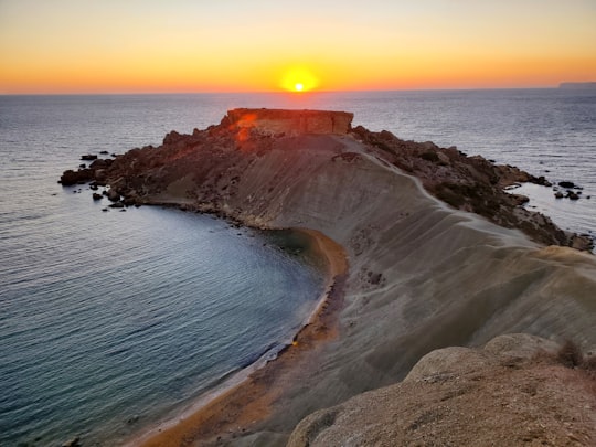 brown rock formation beside body of water during sunset in Għajn Tuffieħa Malta