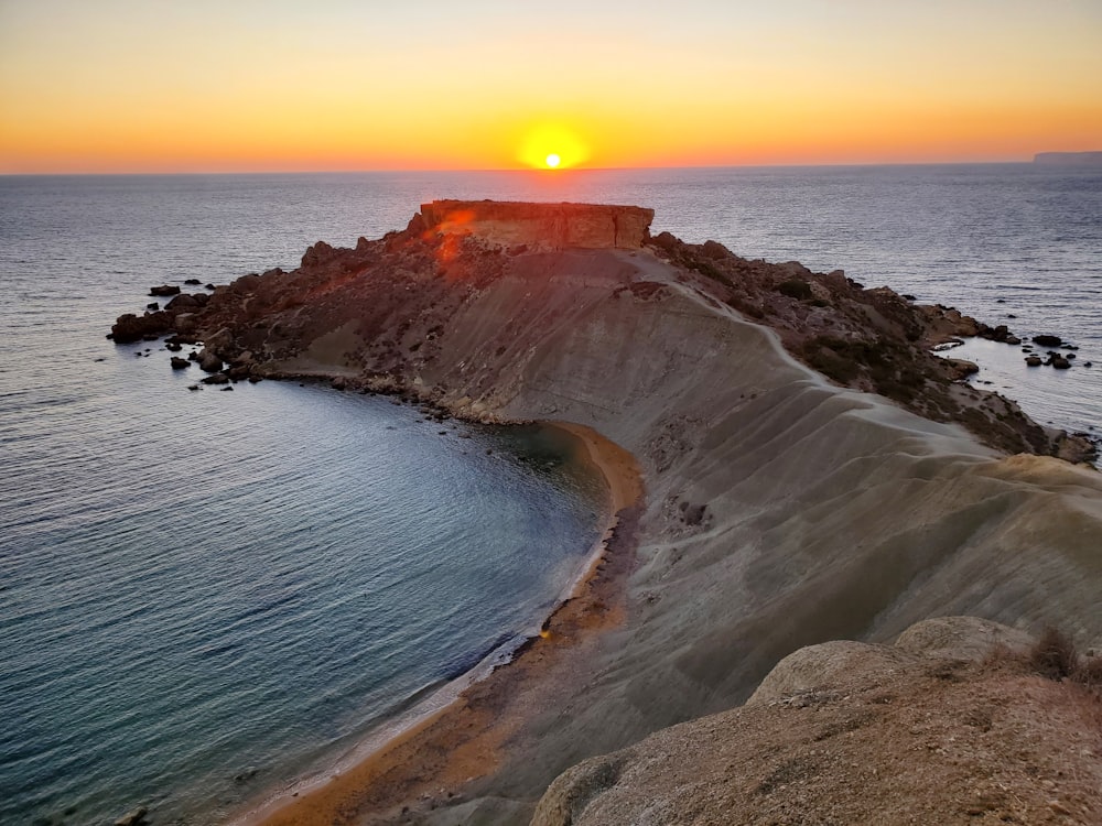 brown rock formation beside body of water during sunset