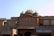 An architectural structure with intricate lattice windows and domed rooftops, displaying a traditional design with earthy tones. The facade features ornate detailing and a symmetrical layout, with Hindi signs visible at the bottom.