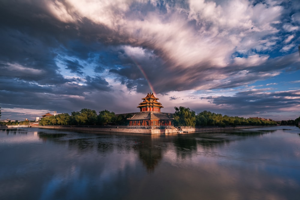 Temple rouge et blanc près du plan d’eau sous un ciel nuageux pendant la journée