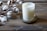 A white candle in a frosted glass container labeled 'shore soap co.' sits on a decorative metal tray. To the left, cotton branches with fluffy white cotton bolls rest on a rustic wooden surface.