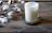 A white candle in a frosted glass container labeled 'shore soap co.' sits on a decorative metal tray. To the left, cotton branches with fluffy white cotton bolls rest on a rustic wooden surface.