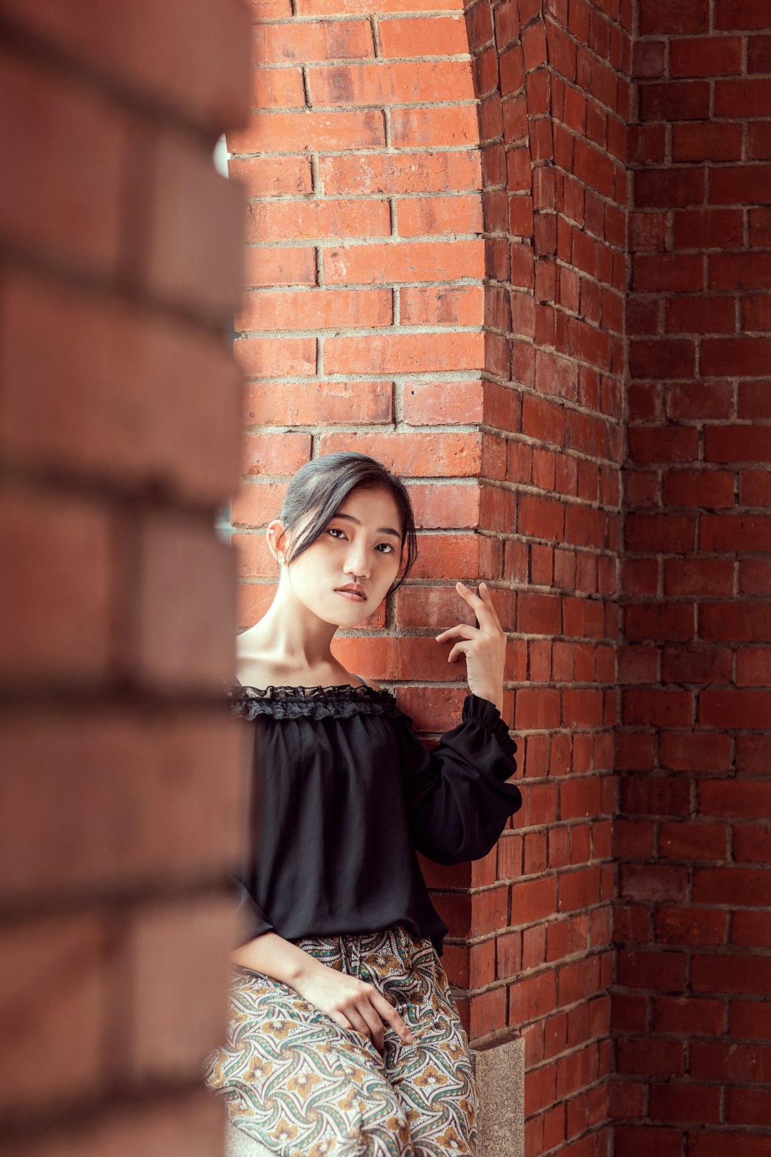 woman in black off shoulder long sleeve shirt standing beside brown brick wall