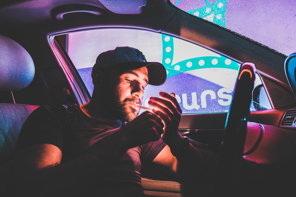 man in black crew neck t-shirt wearing black cap sitting inside car