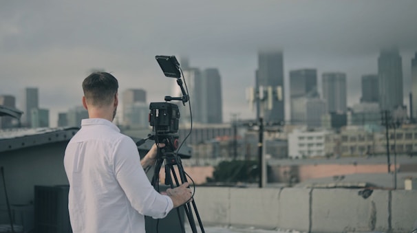 A technician adjusting a nclxcam camera on a rooftop overlooking a cityscape.