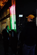 man in black jacket and yellow cap standing near black microphone