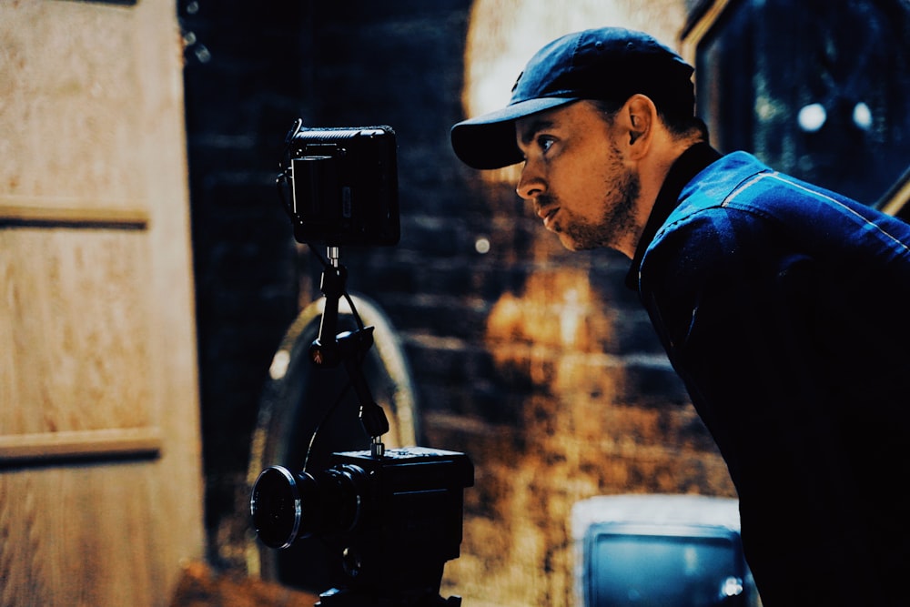 man in blue shirt and black cap holding black camera