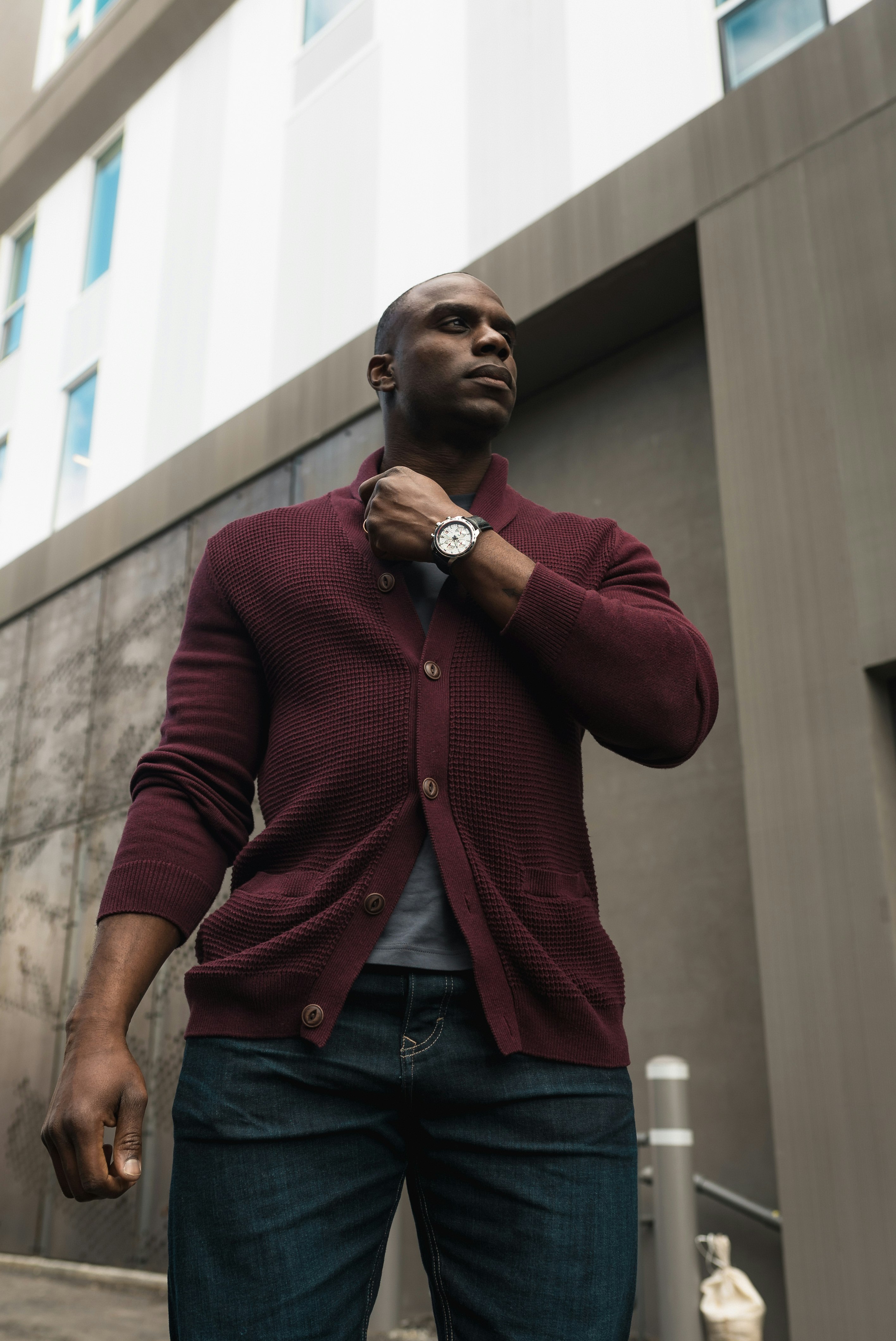 man in maroon button up long sleeve shirt and blue denim jeans standing near white concrete