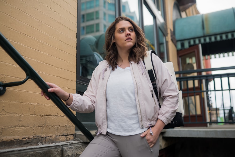 woman in white dress shirt and gray pants standing beside green metal railings during daytime