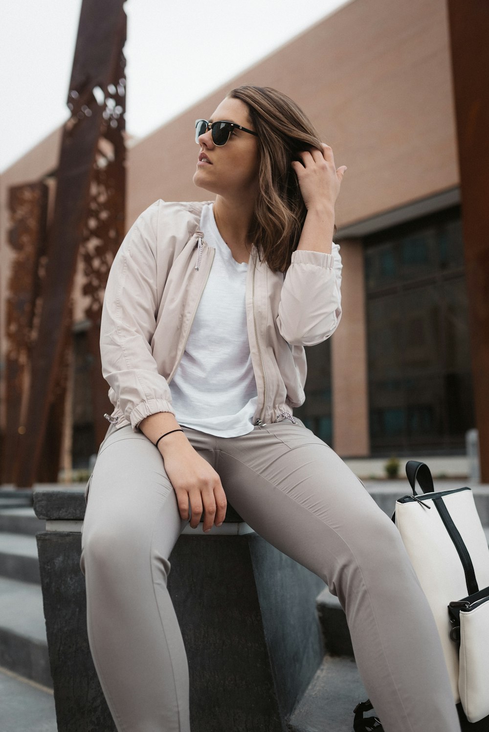 Mujer con camisa blanca de manga larga y pantalones grises sentada en un banco de concreto gris durante el día