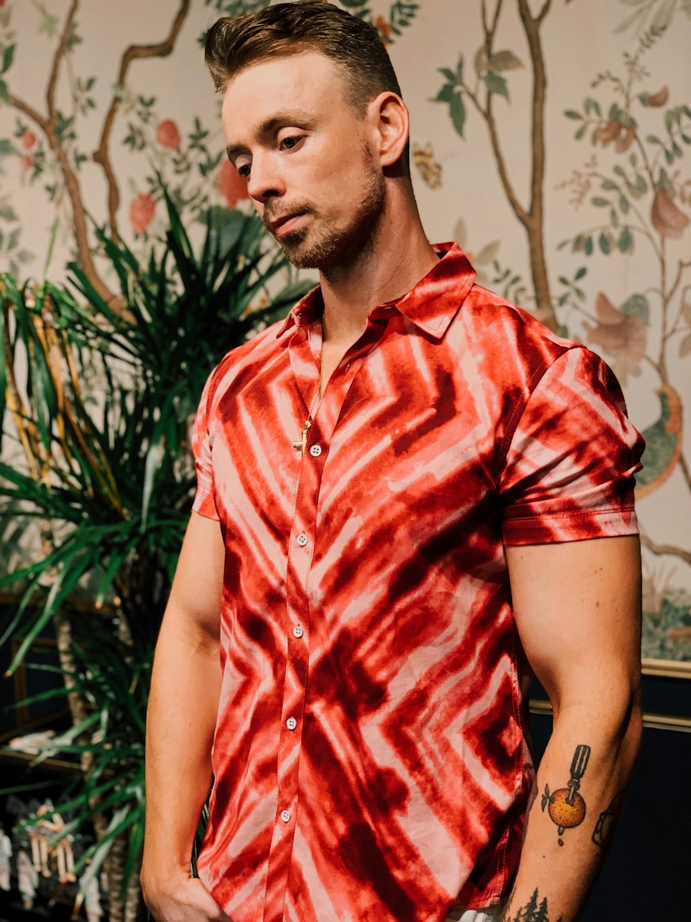 man in red and white plaid button up t-shirt standing near green plant