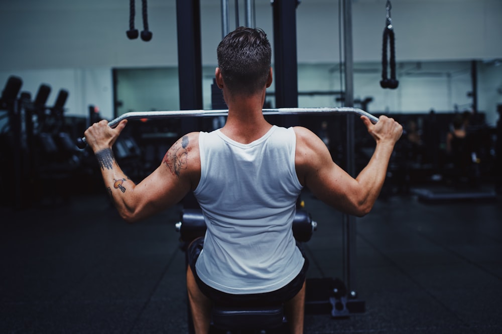 man in gray tank top and black shorts holding black barbell