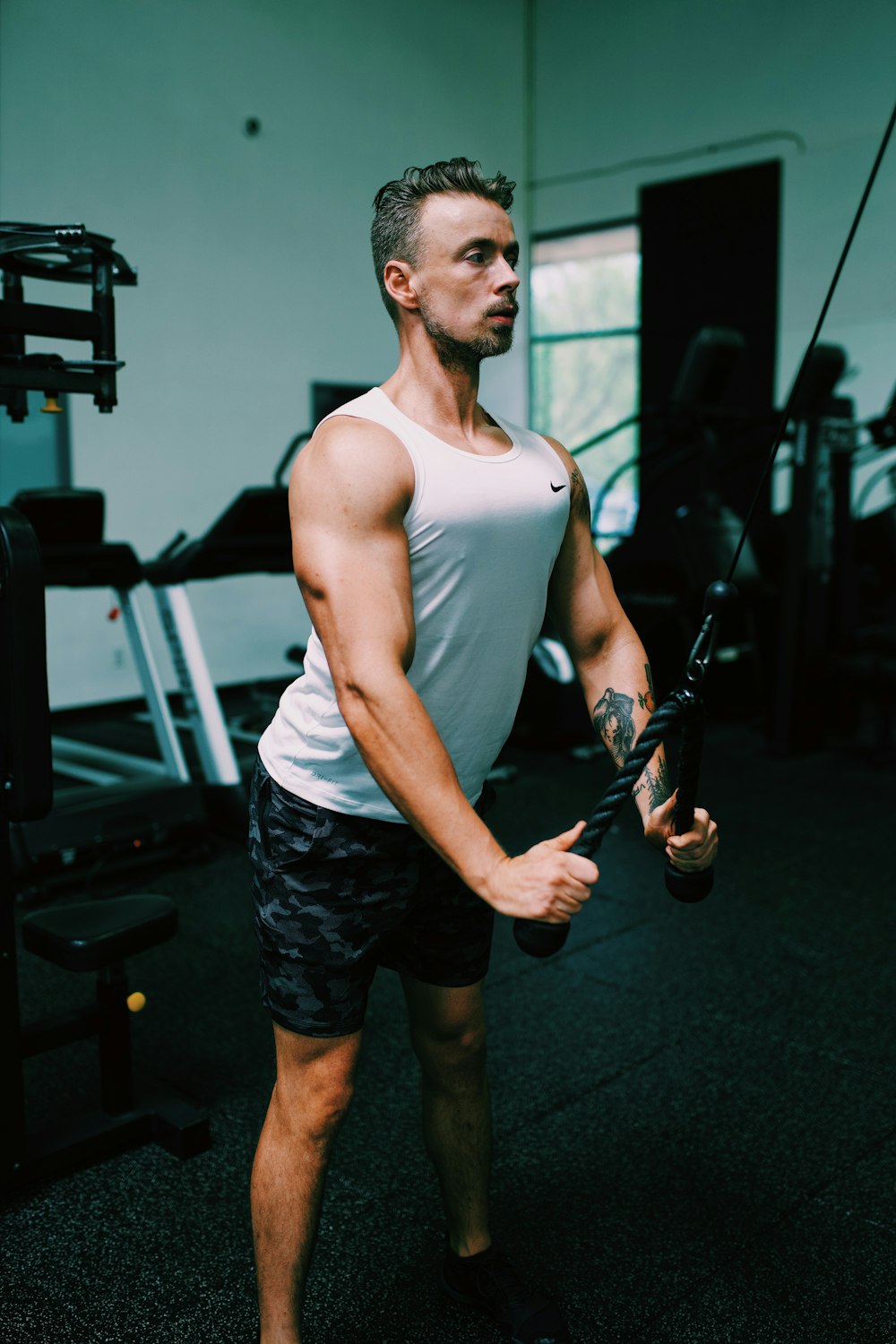 man in white tank top and black shorts holding black and brown rifle