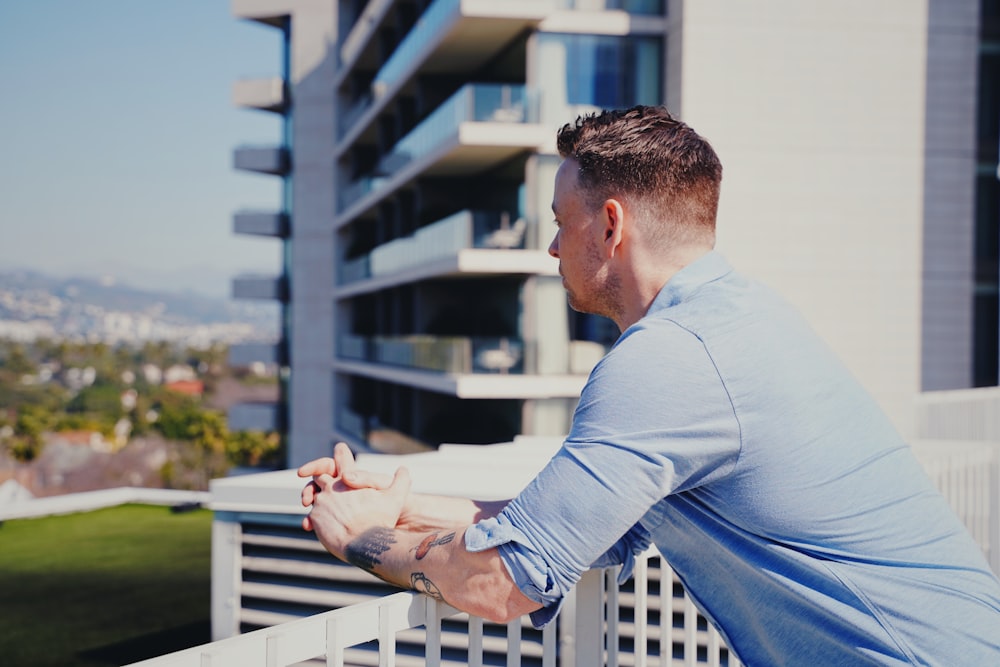 man in blue long sleeve shirt sitting on white wooden fence during daytime