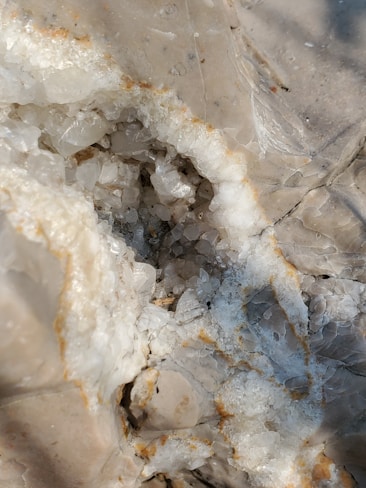 A close-up view of a rough surface exposing translucent crystals embedded in a rocky formation. The crystals exhibit a mix of irregular shapes and are surrounded by a pale, earthy matrix.