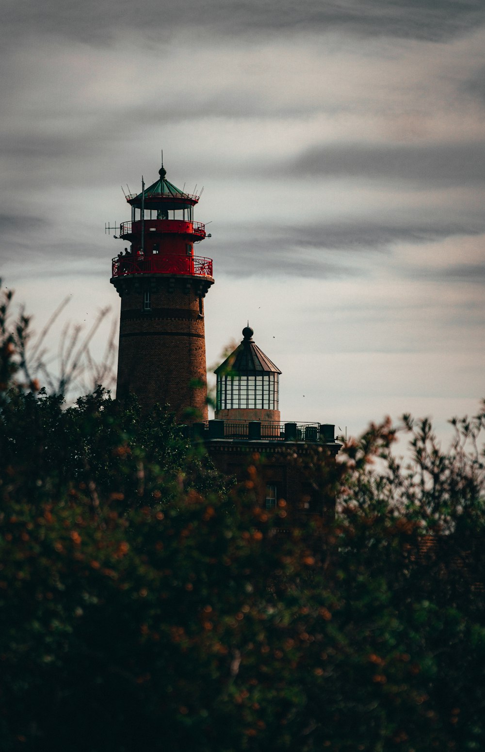red and white lighthouse near green trees under cloudy sky during daytime