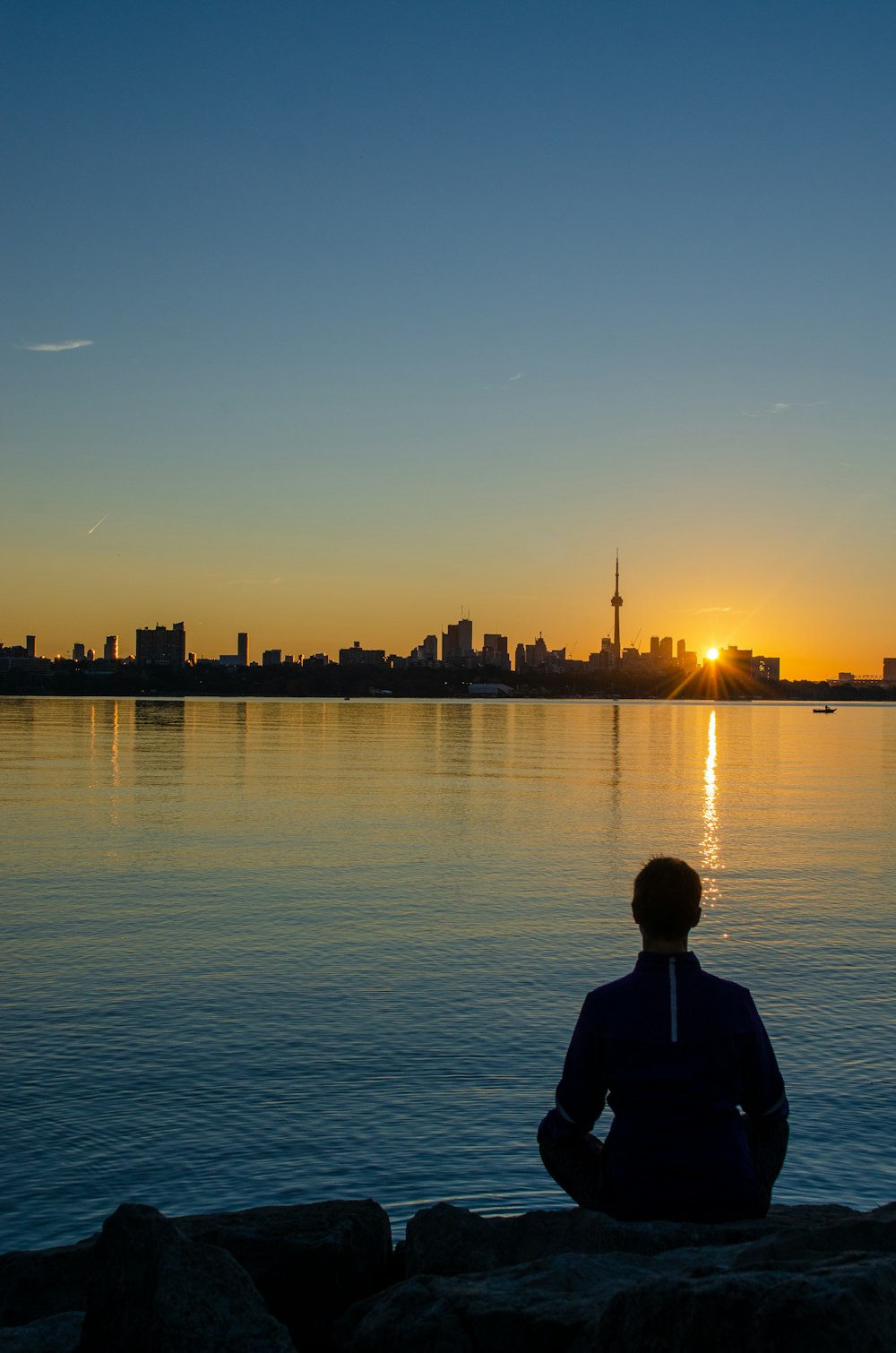 man in black jacket standing near body of water during sunset