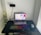 A home office setup with a laptop on a black desk, displaying a webpage. A mechanical keyboard with rainbow backlighting, a mouse with a floral pattern on a mousepad, and a phone mounted on a flexible stand are also present. White flowers are visible on the left side.