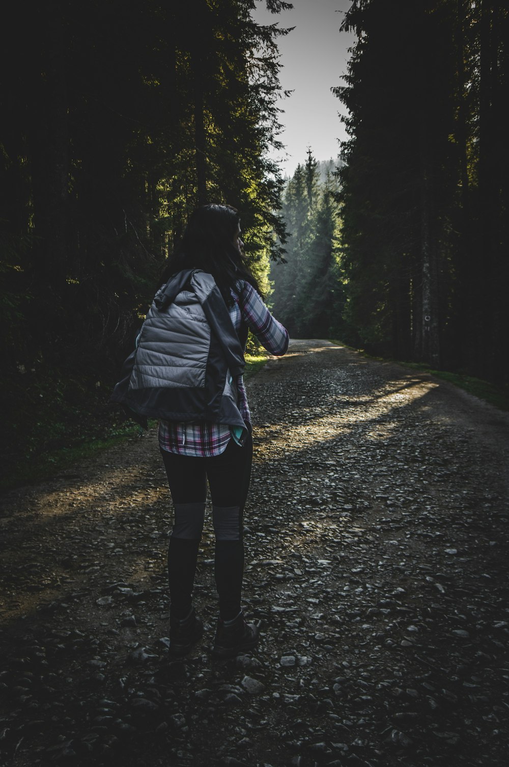 person in black jacket and blue denim jeans standing on pathway in between trees during daytime