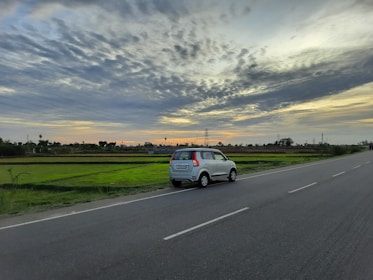 A city car parked on a quiet rural road surrounded by lush greenery under a moody sky.