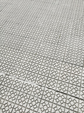 Interlocking stone tiles with a floral pattern cover a large surface, creating a geometric and repetitive design. The light gray stones are arranged in a grid, each featuring a flower motif etched into the surface.