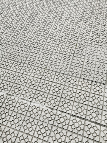 Interlocking stone tiles with a floral pattern cover a large surface, creating a geometric and repetitive design. The light gray stones are arranged in a grid, each featuring a flower motif etched into the surface.