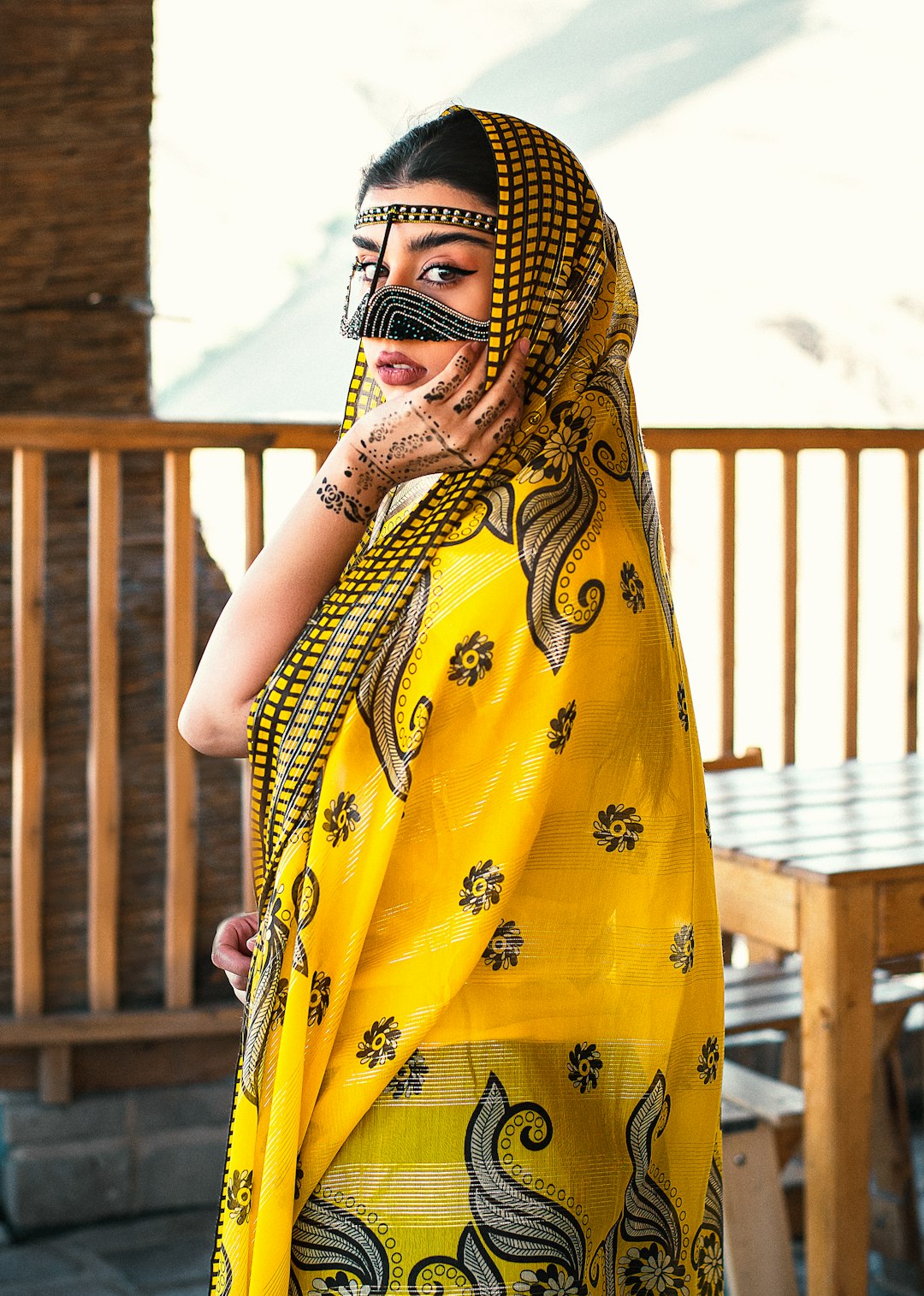 woman in yellow and black floral hijab standing near brown wooden fence during daytime