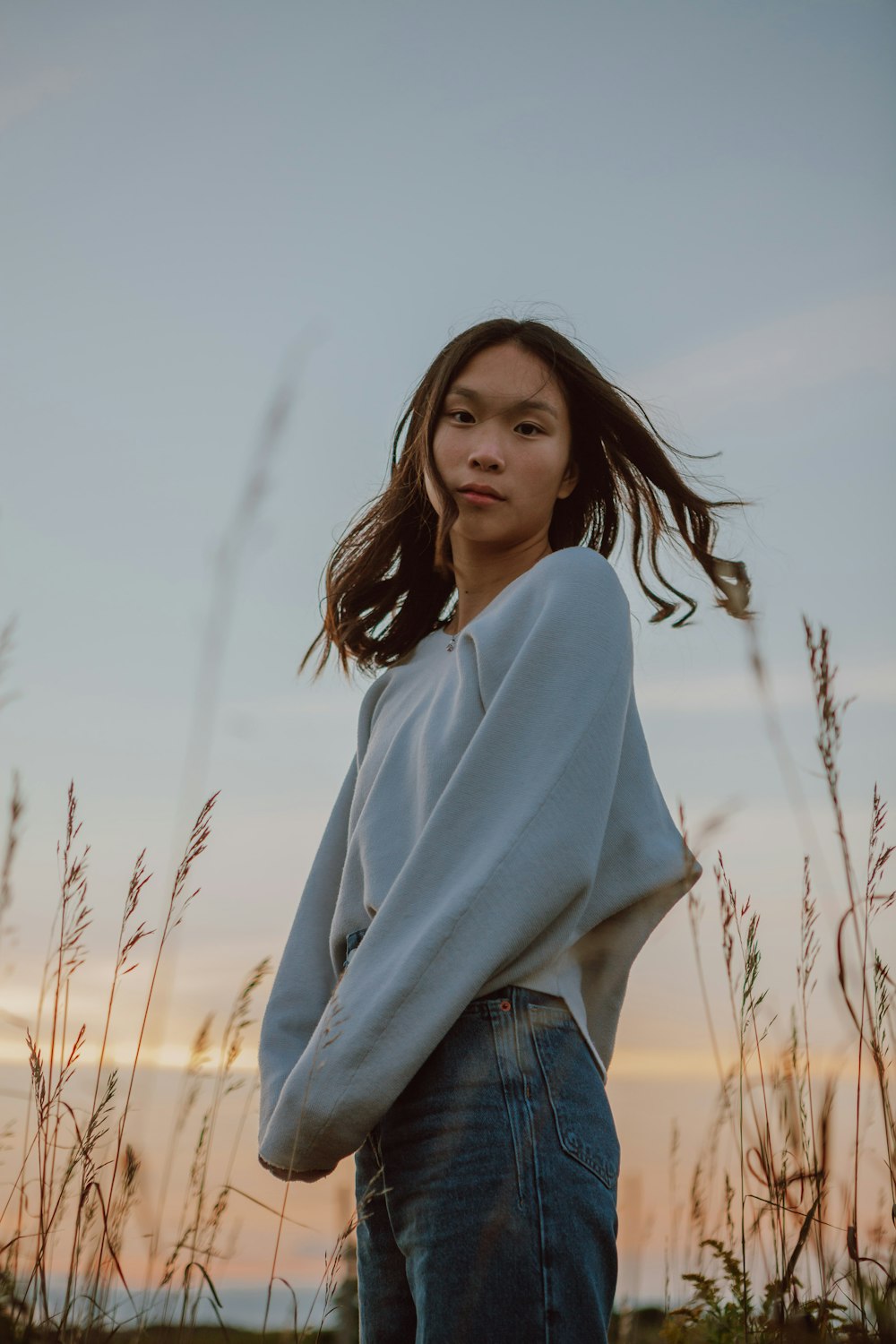 woman in gray long sleeve shirt standing on brown grass field during daytime