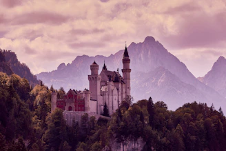 A richly detailed concept art of a towering ancient castle nestled among misty mountains at dawn.