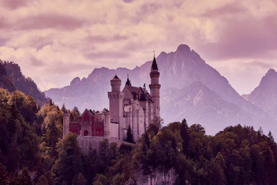 A richly detailed concept art of a towering ancient castle nestled among misty mountains at dawn.