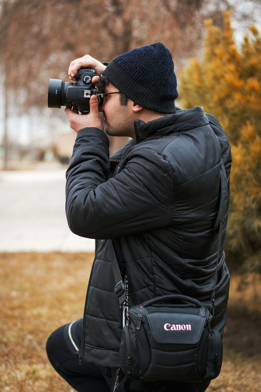 man in black jacket and knit cap holding black dslr camera