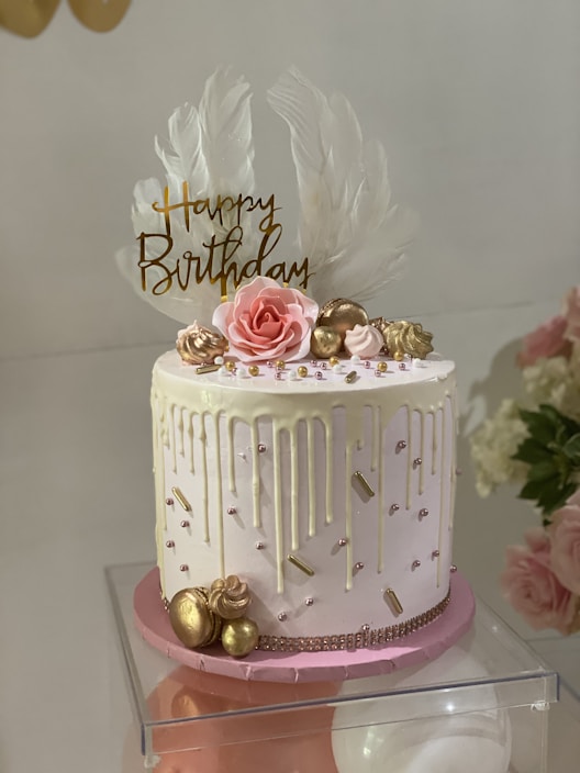 A beautifully decorated birthday cake with pastel pink roses and delicate piping on a wooden table
