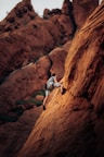 man in white t-shirt climbing brown rock mountain during daytime