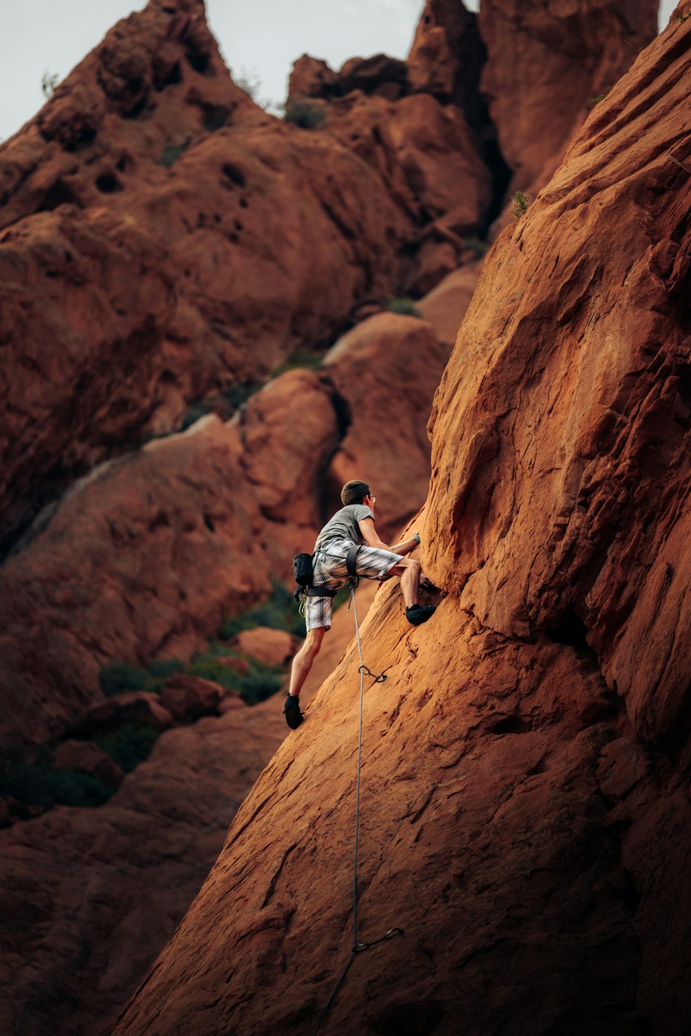 Hombre con camiseta blanca escalando la montaña de roca marrón durante el día
