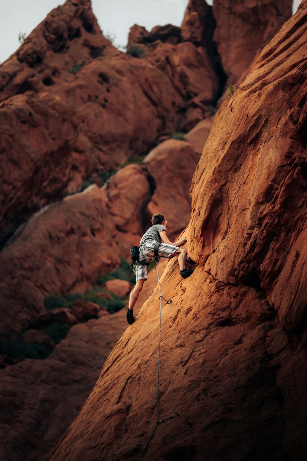 homme en t-shirt blanc escalade montagne rocheuse marron pendant la journée