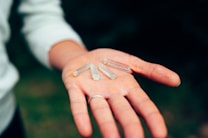 A hand is holding several small, clear crystal-like objects. The person's palm is open, and the items are placed neatly. The background is blurred, focusing on the hand and crystals.