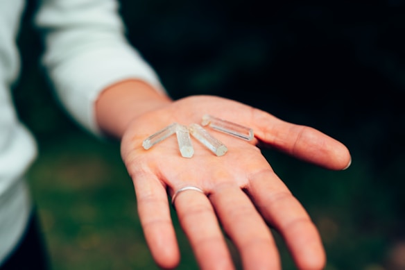 A hand is holding several small, clear crystal-like objects. The person's palm is open, and the items are placed neatly. The background is blurred, focusing on the hand and crystals.