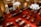 An ornate legislative chamber features rows of wooden desks and chairs placed over a richly patterned red carpet. The room is adorned with large chandeliers and elegant columns, with an American flag and another flag near the podium at the front. The high ceiling and intricate details add a sense of historical grandeur.
